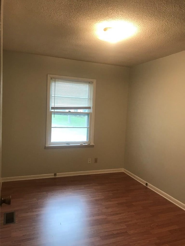 empty room with a textured ceiling, dark wood finished floors, visible vents, and baseboards