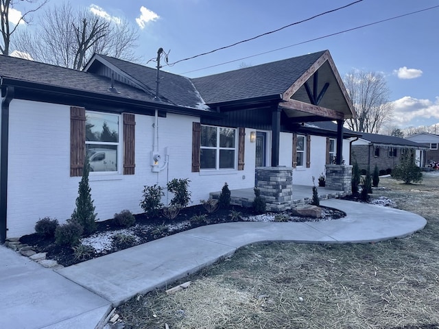 view of front of house with a shingled roof, covered porch, and brick siding