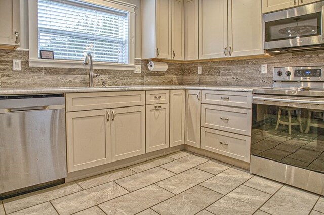 kitchen featuring light stone counters, light tile patterned flooring, a sink, appliances with stainless steel finishes, and decorative backsplash