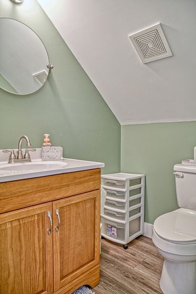 bathroom featuring visible vents, toilet, vaulted ceiling, vanity, and wood finished floors