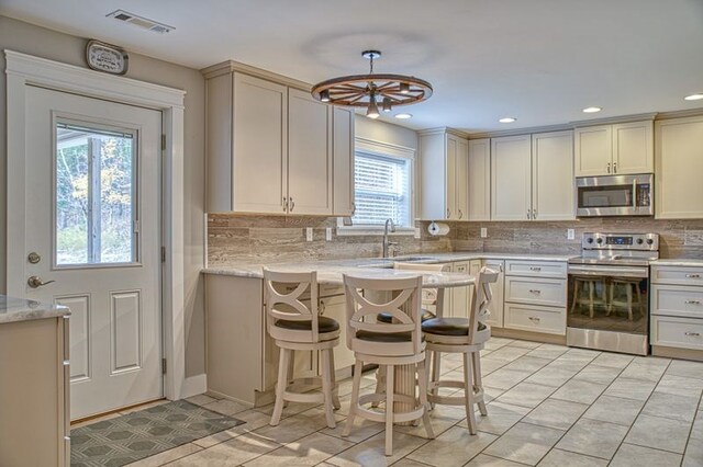 kitchen featuring a breakfast bar, visible vents, appliances with stainless steel finishes, a sink, and light stone countertops