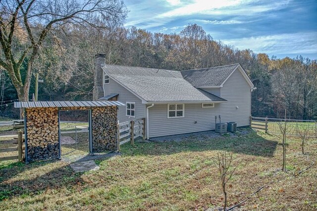 view of home's exterior with roof with shingles, a chimney, central air condition unit, a lawn, and fence