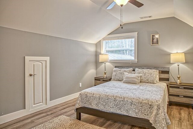 bedroom featuring ceiling fan, wood finished floors, visible vents, baseboards, and vaulted ceiling