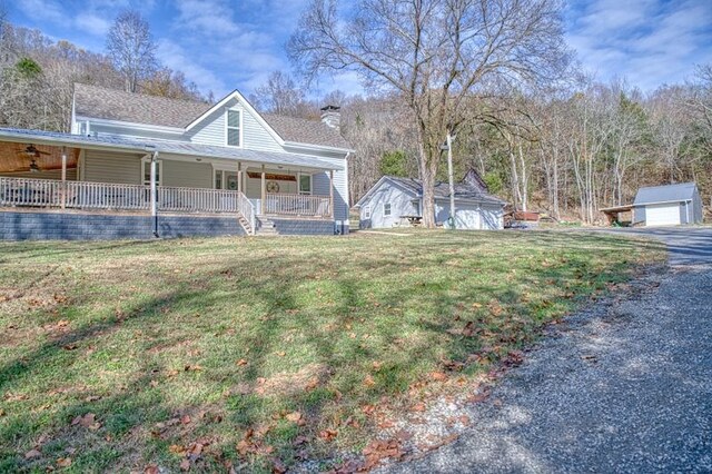 view of front of home featuring covered porch, a chimney, a front lawn, and an outdoor structure