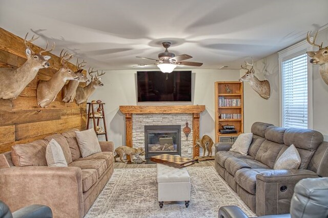 living area with ceiling fan, a stone fireplace, and light wood finished floors