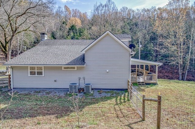 back of house featuring central AC unit, a lawn, a chimney, roof with shingles, and a deck