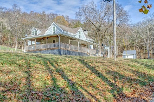 country-style home featuring a porch, a garage, an outdoor structure, a storage unit, and a front yard