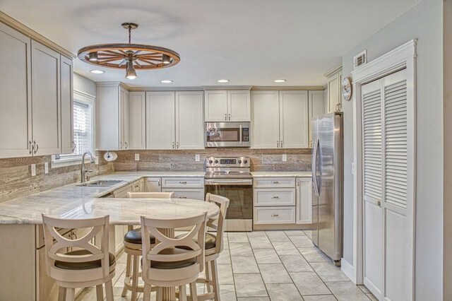 kitchen with stainless steel appliances, a peninsula, a sink, backsplash, and decorative light fixtures