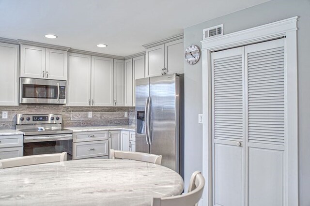 kitchen featuring recessed lighting, visible vents, appliances with stainless steel finishes, backsplash, and light stone countertops