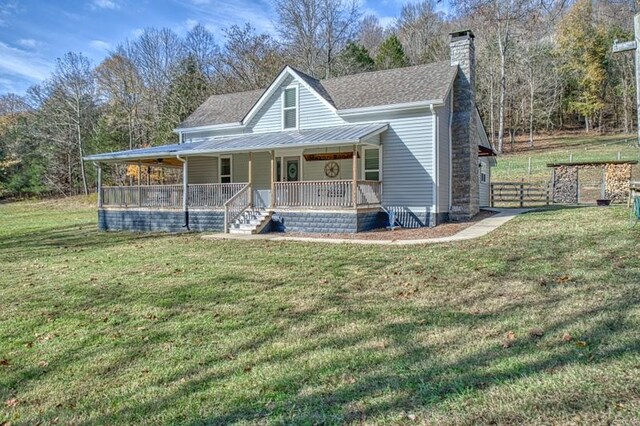 country-style home with a porch, a chimney, a front yard, and a shingled roof