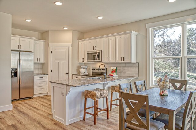 kitchen with light wood finished floors, white cabinets, light stone counters, a peninsula, and stainless steel appliances