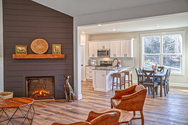 living area with light wood-style floors, vaulted ceiling, a fireplace, and baseboards