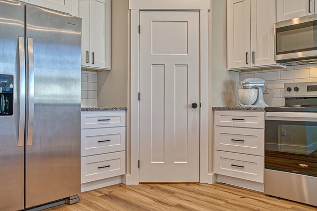 kitchen with light wood finished floors, tasteful backsplash, dark stone counters, stainless steel appliances, and white cabinetry