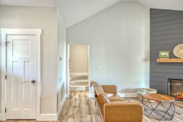 sitting room with baseboards, light wood-style flooring, stairway, a fireplace, and high vaulted ceiling