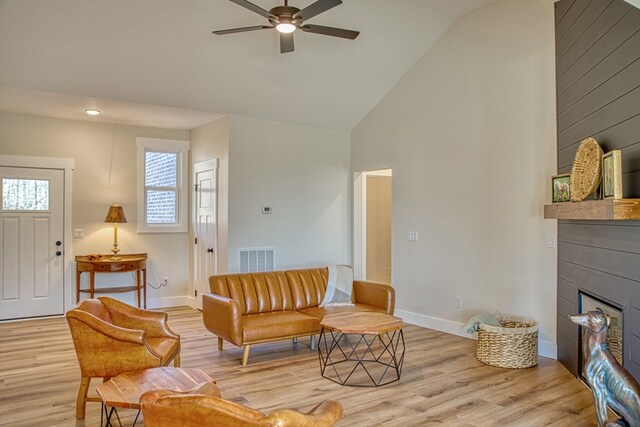 living room with high vaulted ceiling, light wood-type flooring, a large fireplace, and visible vents