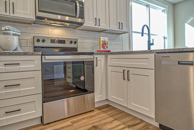 kitchen featuring appliances with stainless steel finishes, light wood-style flooring, white cabinetry, and decorative backsplash