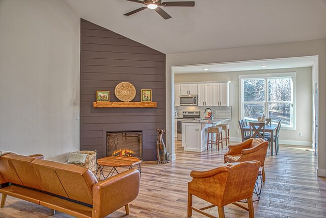 living room with a fireplace, light wood-style flooring, baseboards, and ceiling fan