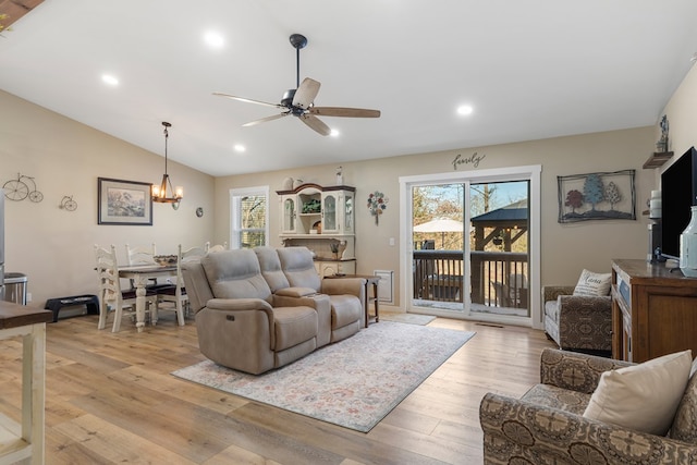 living area with light wood-style floors, vaulted ceiling, plenty of natural light, and ceiling fan with notable chandelier