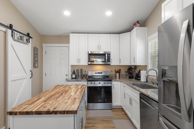 kitchen featuring a barn door, butcher block countertops, a sink, white cabinets, and appliances with stainless steel finishes