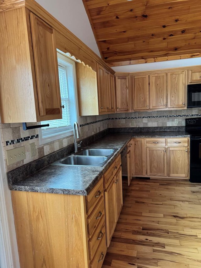 kitchen with a sink, light wood-style floors, vaulted ceiling, black appliances, and dark countertops