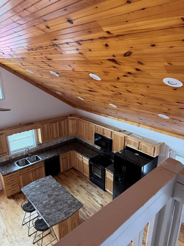 kitchen with a breakfast bar area, a sink, vaulted ceiling, a center island, and black appliances