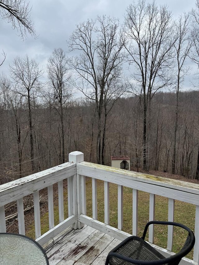 wooden deck with an outbuilding, a lawn, a forest view, and a shed