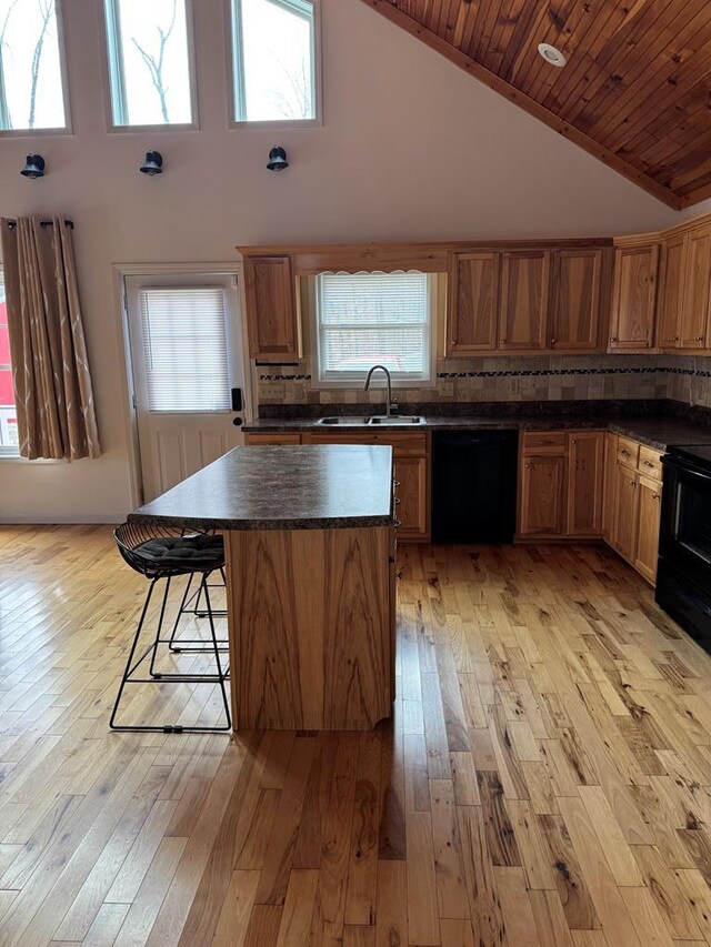 kitchen featuring a sink, a kitchen breakfast bar, a center island, black appliances, and dark countertops