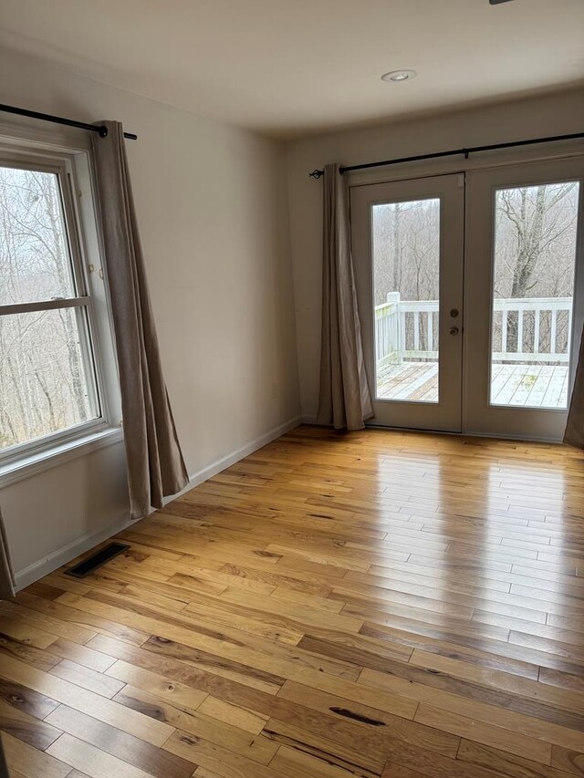 unfurnished room featuring light wood-style floors, french doors, visible vents, and baseboards