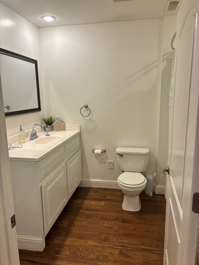 half bathroom with visible vents, baseboards, toilet, wood finished floors, and vanity