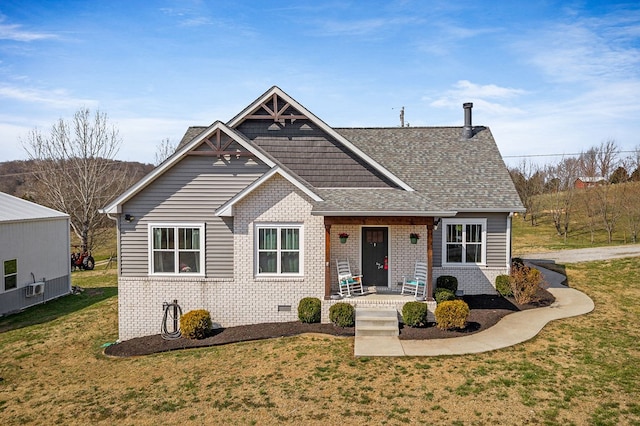 view of front of house with a front yard, a porch, brick siding, and roof with shingles