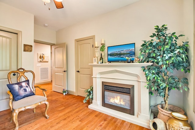 sitting room with ceiling fan, a glass covered fireplace, wood finished floors, and visible vents