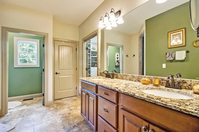 bathroom featuring a walk in closet, a sink, baseboards, and double vanity