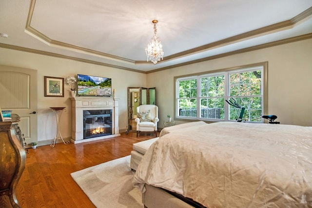 bedroom with a chandelier, wood finished floors, a raised ceiling, a glass covered fireplace, and crown molding