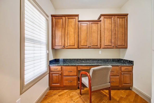 home office featuring light wood finished floors, baseboards, and built in study area