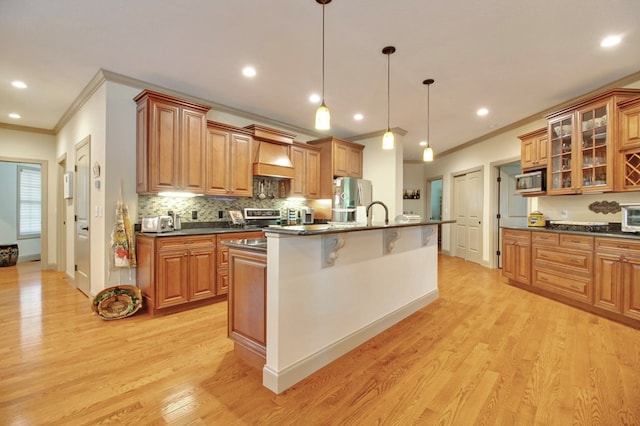 kitchen featuring brown cabinets, decorative light fixtures, a center island with sink, glass insert cabinets, and appliances with stainless steel finishes