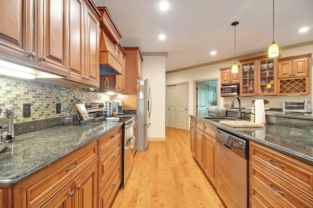 kitchen with decorative light fixtures, a sink, appliances with stainless steel finishes, brown cabinetry, and glass insert cabinets