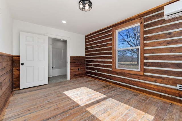 interior space with light wood-type flooring, wainscoting, a wall mounted air conditioner, and wood walls