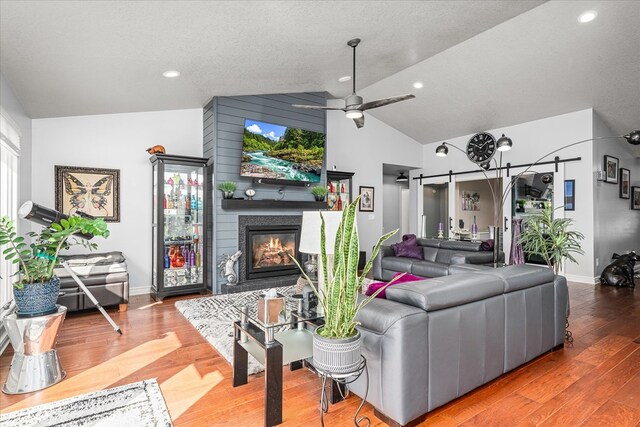 living room featuring lofted ceiling, a barn door, a ceiling fan, a large fireplace, and wood finished floors