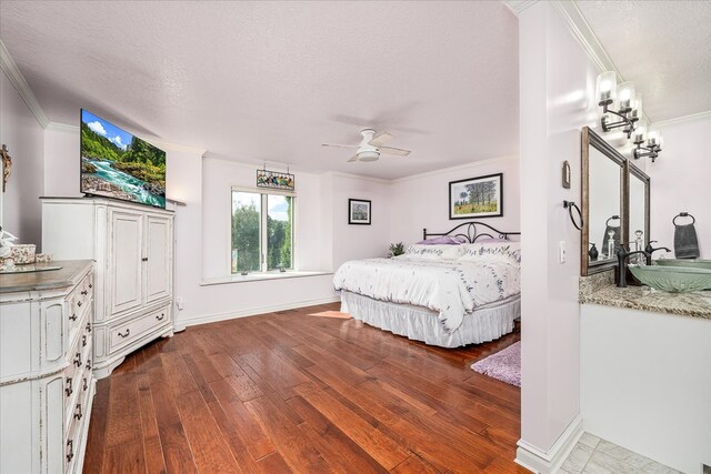 bedroom featuring baseboards, wood finished floors, a textured ceiling, crown molding, and a sink