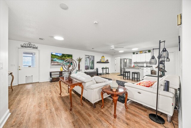 living room with a textured ceiling, ceiling fan, light wood-style flooring, and baseboards