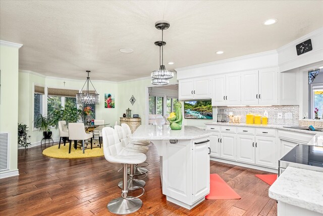 kitchen with tasteful backsplash, white cabinets, a kitchen island, an inviting chandelier, and pendant lighting