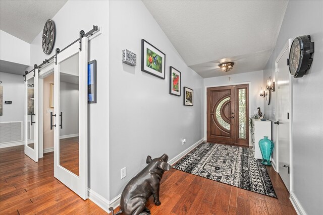 foyer featuring visible vents, a barn door, a textured ceiling, wood finished floors, and baseboards