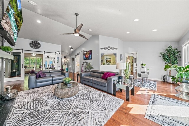 living room featuring a barn door, wood finished floors, a ceiling fan, baseboards, and vaulted ceiling