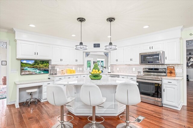 kitchen featuring appliances with stainless steel finishes, white cabinetry, hanging light fixtures, and ornamental molding