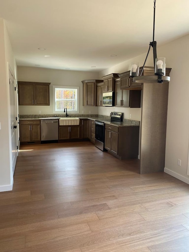 kitchen with decorative light fixtures, light wood finished floors, appliances with stainless steel finishes, a sink, and dark brown cabinets