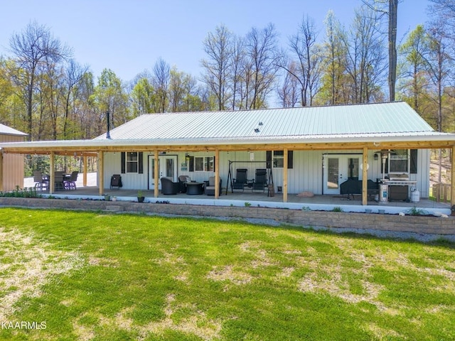 back of house featuring a yard, a patio, outdoor lounge area, board and batten siding, and metal roof