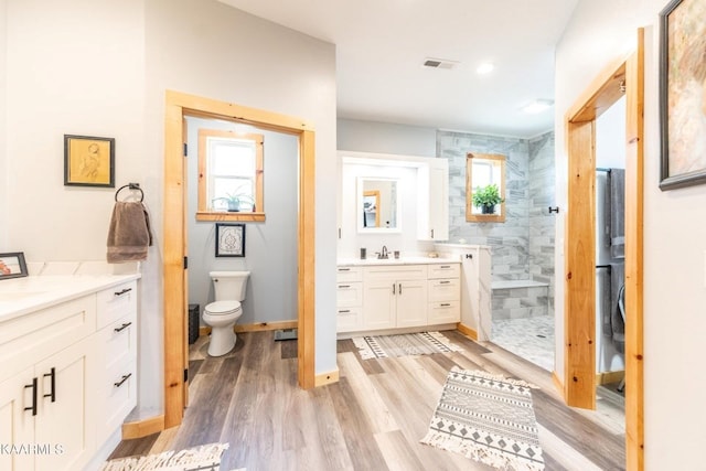 full bathroom featuring visible vents, toilet, vanity, wood finished floors, and walk in shower