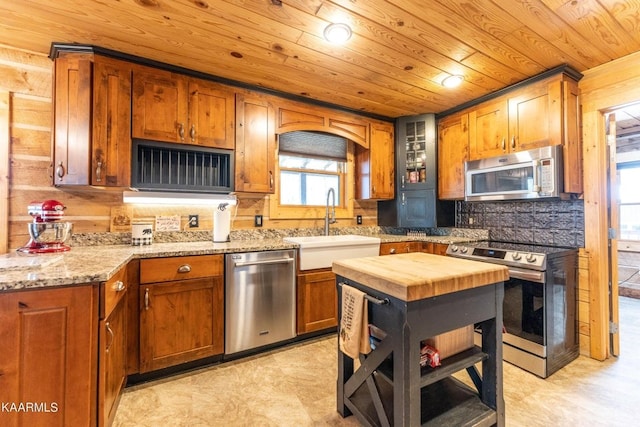 kitchen with light stone counters, brown cabinets, appliances with stainless steel finishes, wood ceiling, and a sink