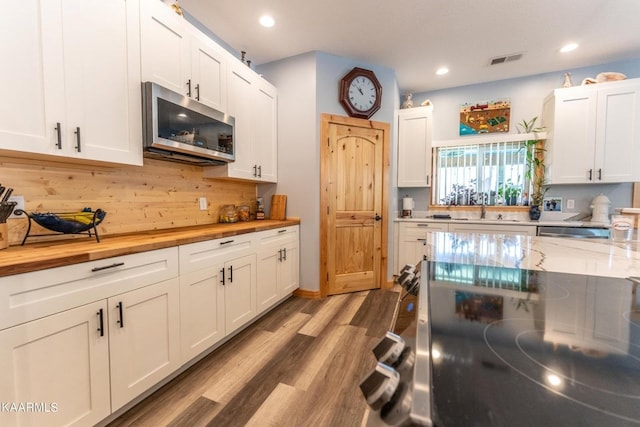 kitchen featuring butcher block countertops, white cabinets, stainless steel microwave, and wood finished floors