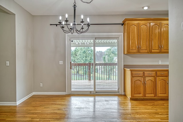 unfurnished dining area with a notable chandelier, light wood finished floors, and baseboards